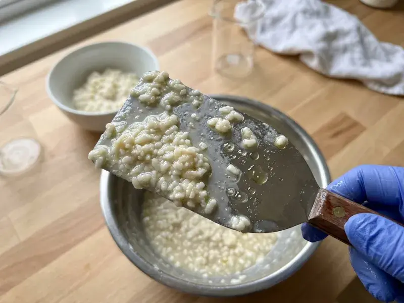Soap batter in a pot with small rice-sized lumps floating in thinner, oily liquid